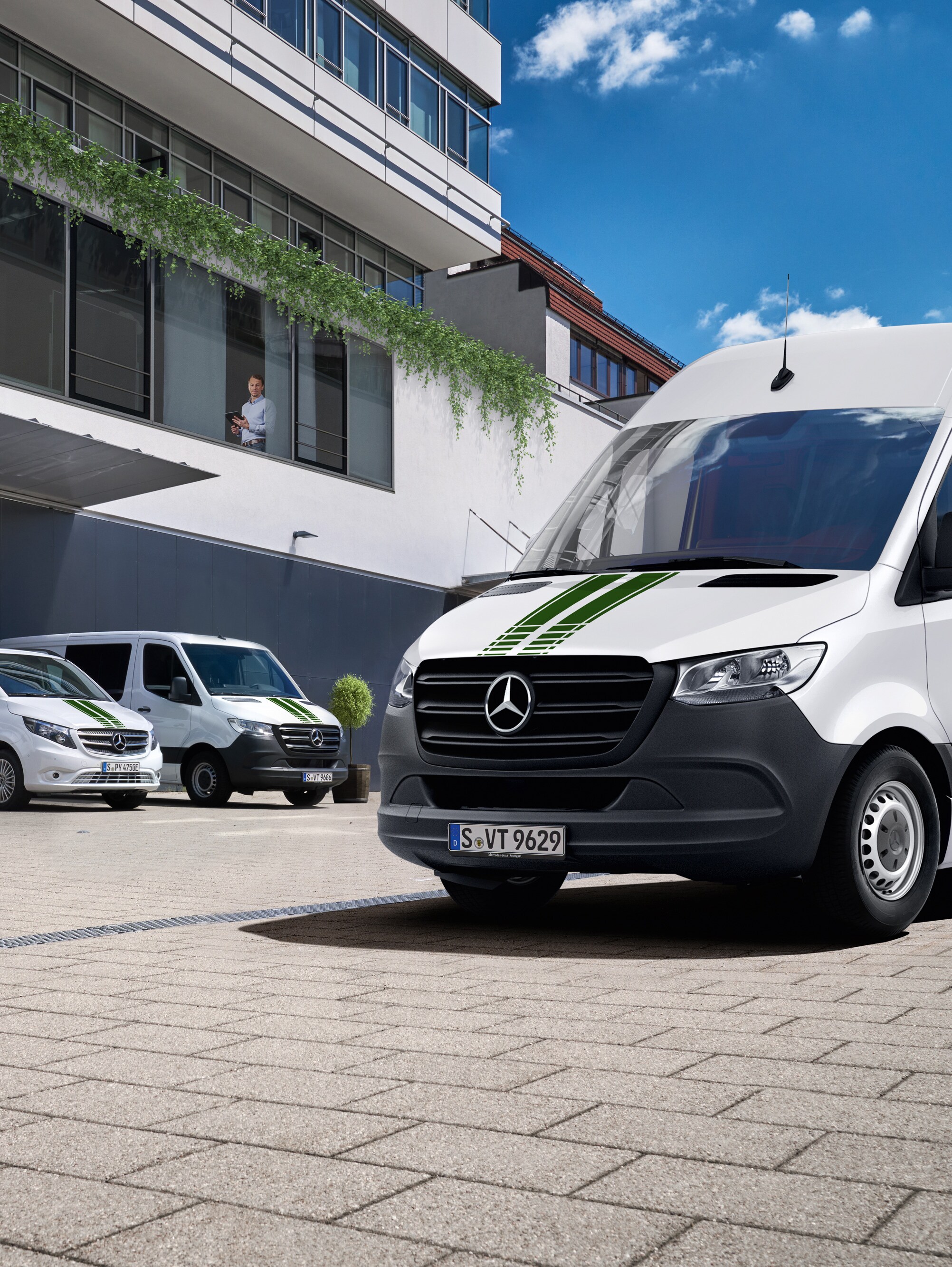Een wagenpark witte Mercedes-Benz bedrijfswagens voor een kantoorgebouw op een zonnige dag met blauwe lucht.