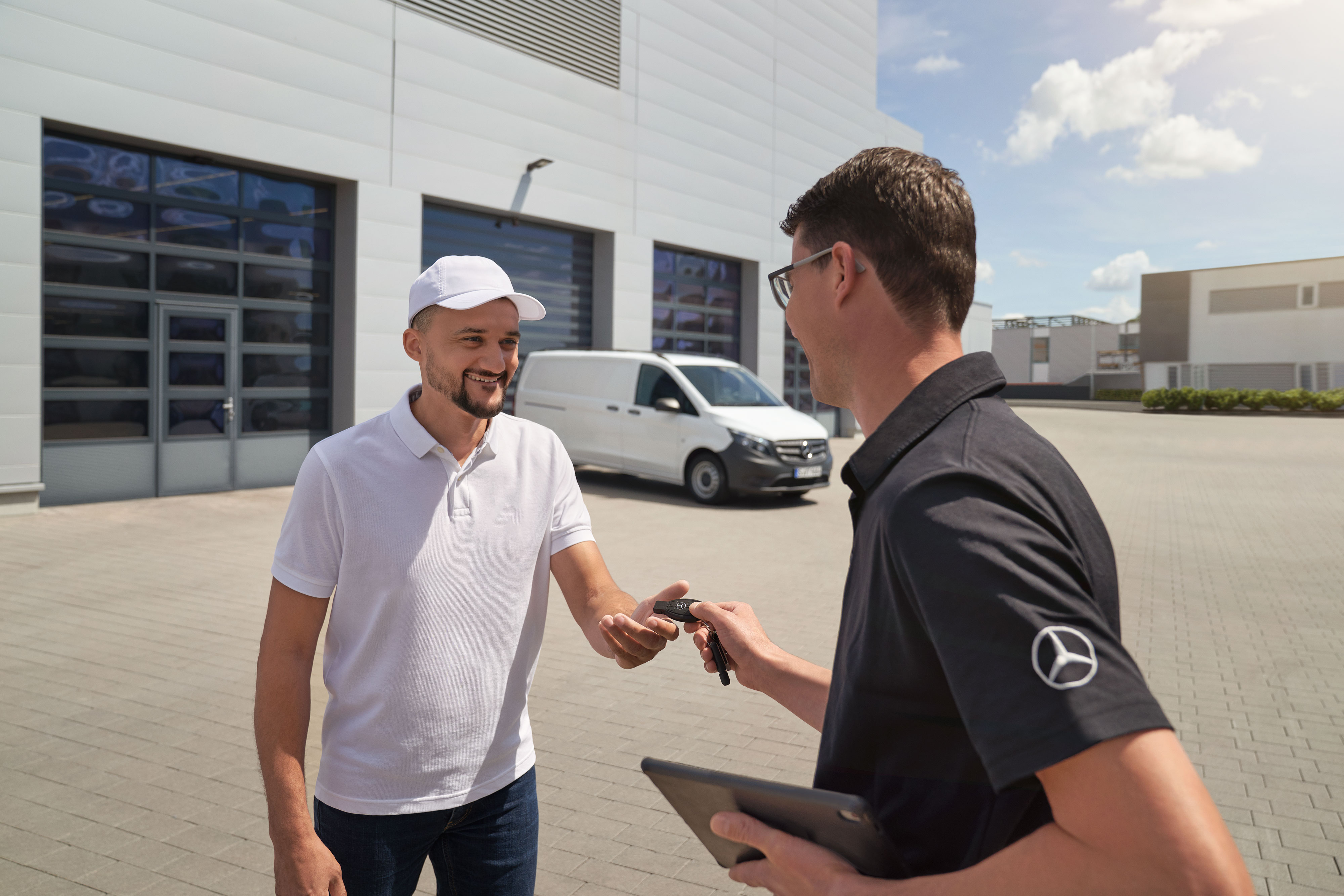Mercedes-Benz | Maintenance | Enlèvement et livraison Représentant SAV Mercedes-Benz remettant les clés à un client, avec un utilitaire léger Mercedes-Benz Vito blanc à l'arrière-plan.