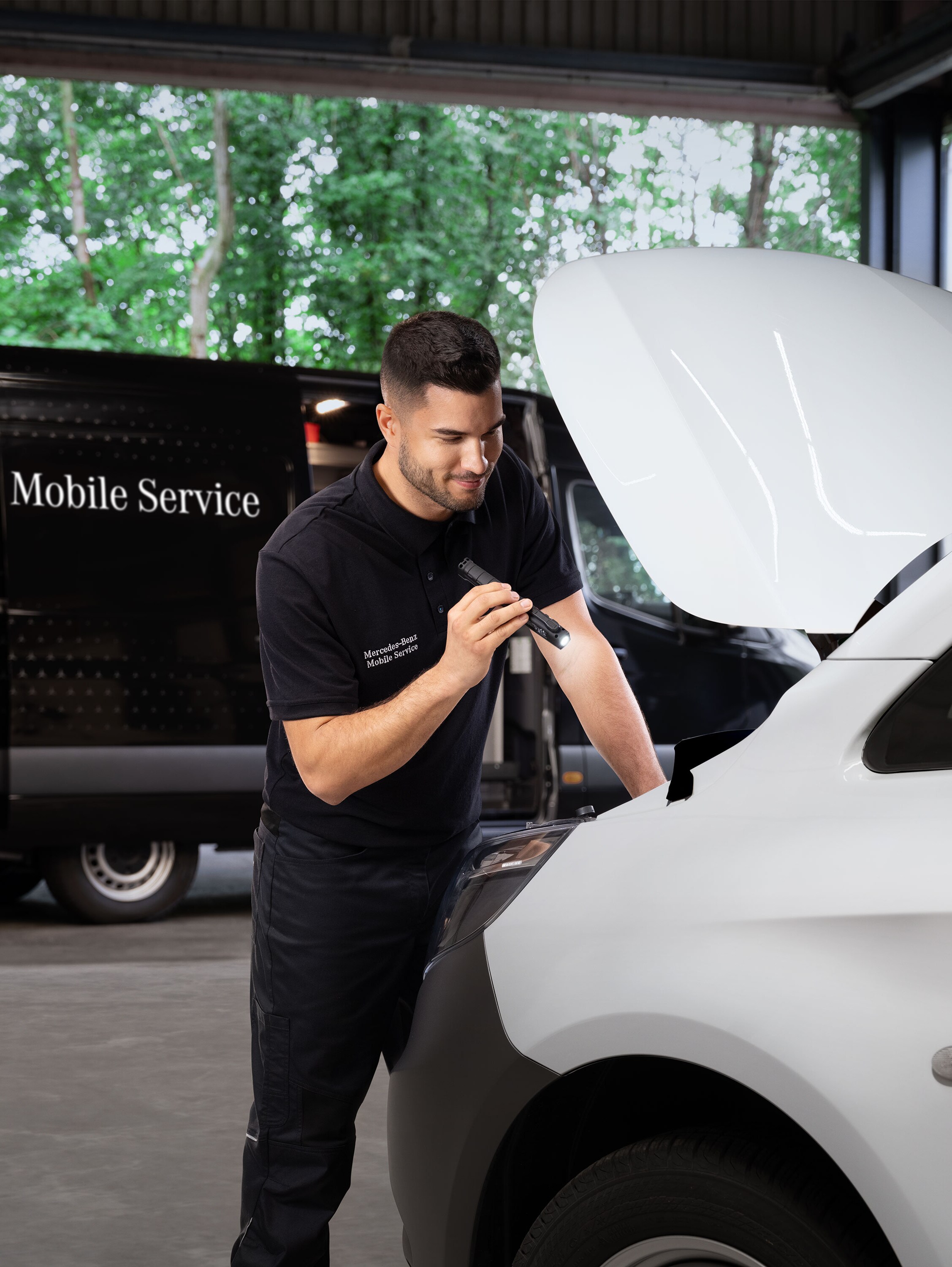 Monteur inspecteert de motor van een witte Mercedes-Benz bedrijfswagen.