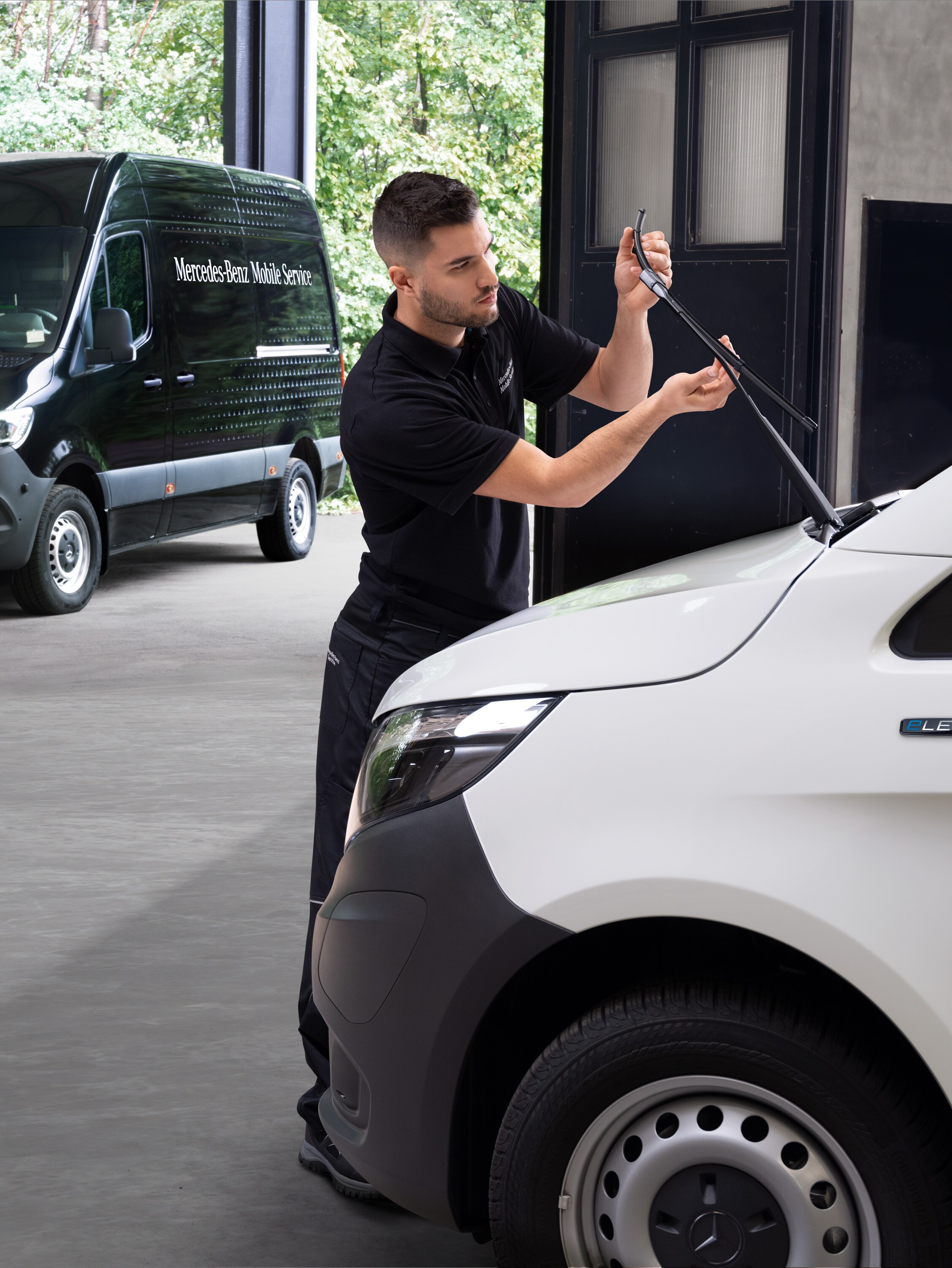 Een monteur vervangt ruitenwisserbladen op een witte Mercedes-Benz Vito bestelwagen.