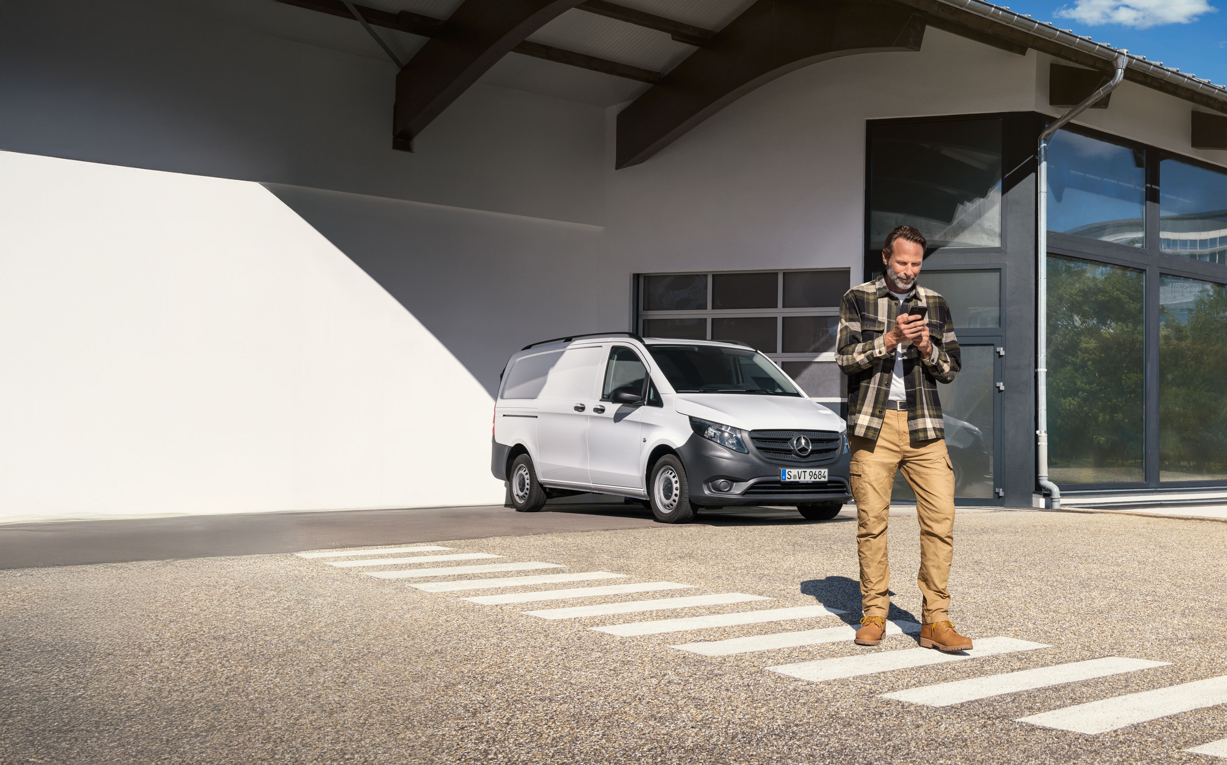 Mercedes-Benz | Maintenance | Prise de rendez-vous Un client prend rendez-vous depuis son mobile, devant un Mercedes-Benz Vito blanc.