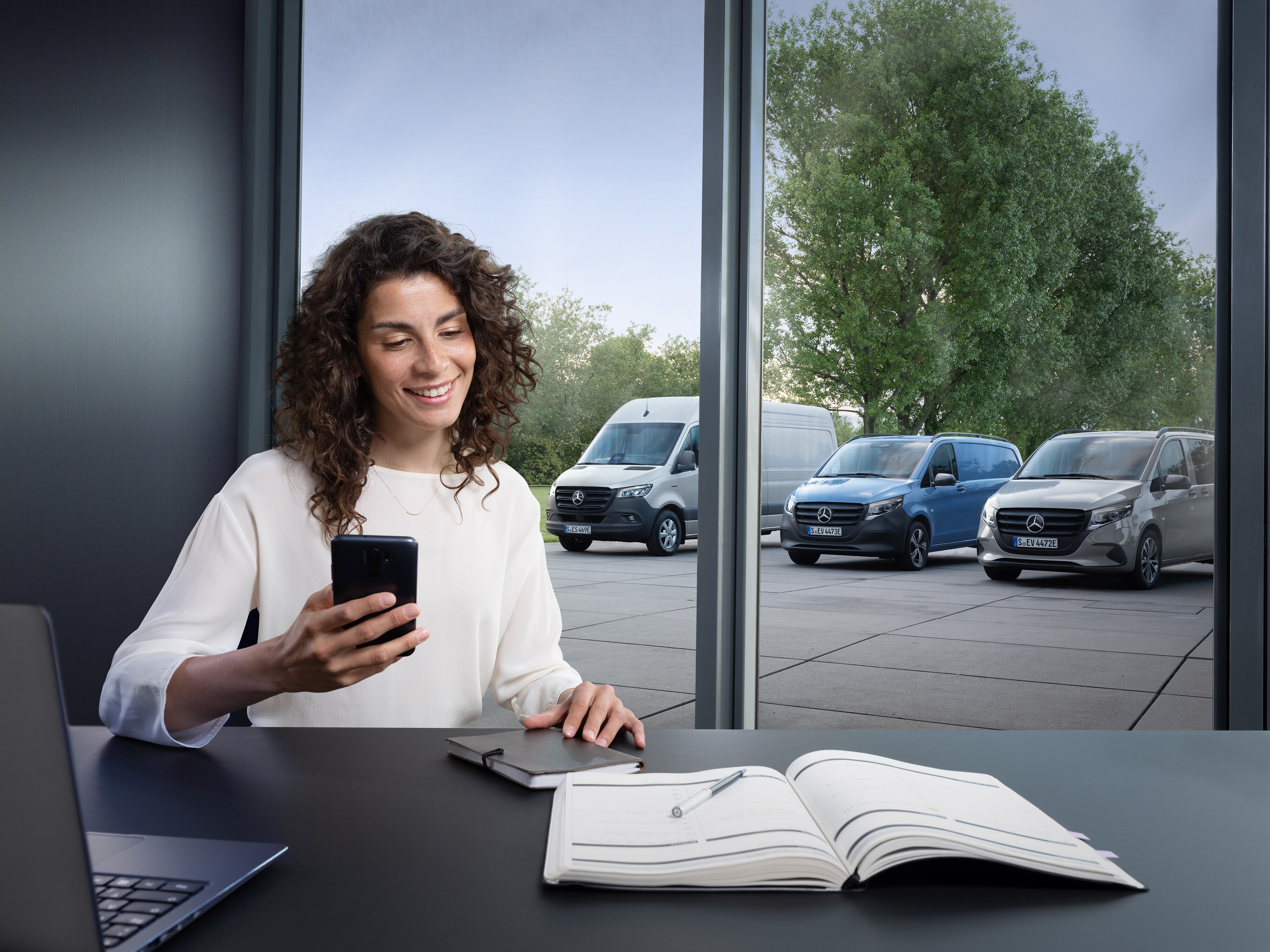 Vrouw plant op haar smartphone een afspraak, met een reeks Mercedes-Benz Bedrijfswagens op de achtergrond.