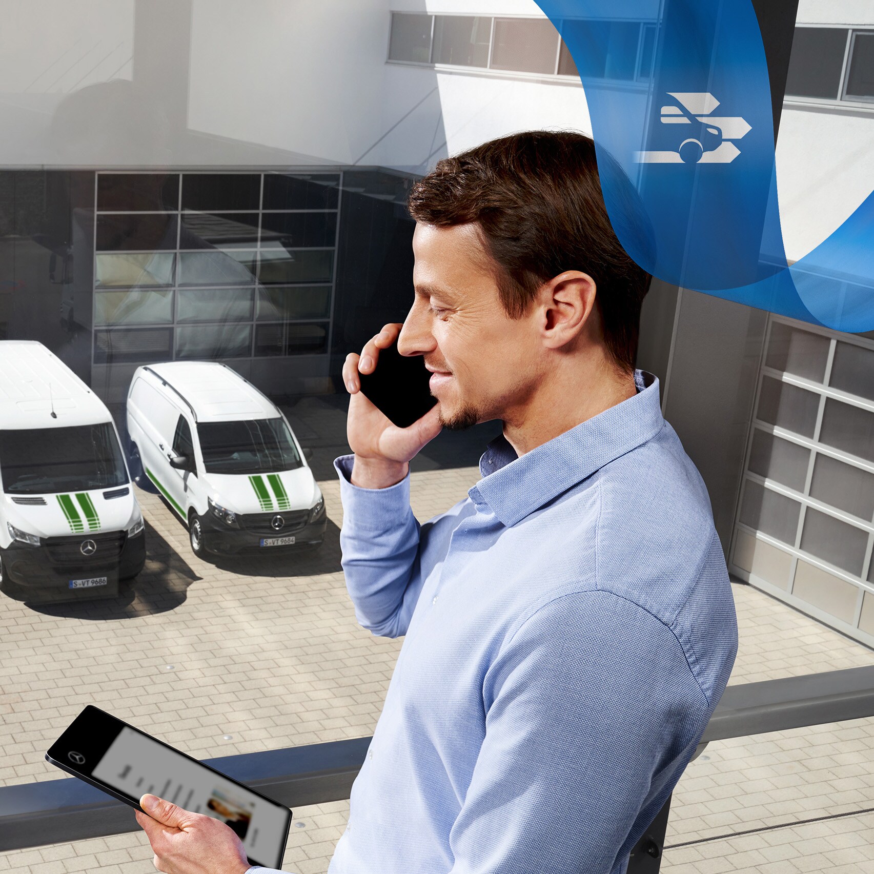 Een man telefoneert terwijl hij naar een tablet kijkt, met een reeks Mercedes-Benz bedrijfswagens op de achtergrond.