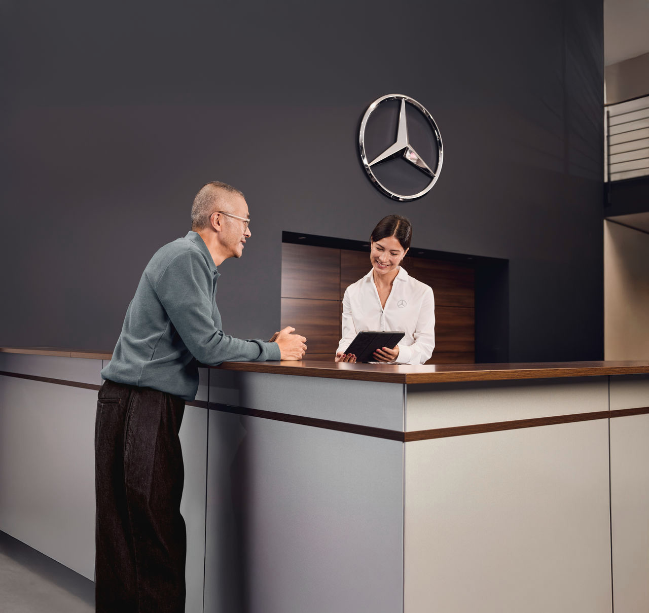 Klant ontvangt ondersteuning aan de Mercedes-Benz receptie Klant wordt geholpen door een medewerker aan de receptiebalie van een Mercedes-Benz vestiging.
